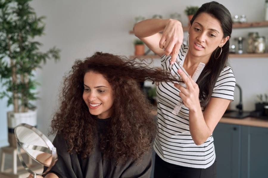 Hairstylist helping client choose haircut while styling curly hair in modern salon setting