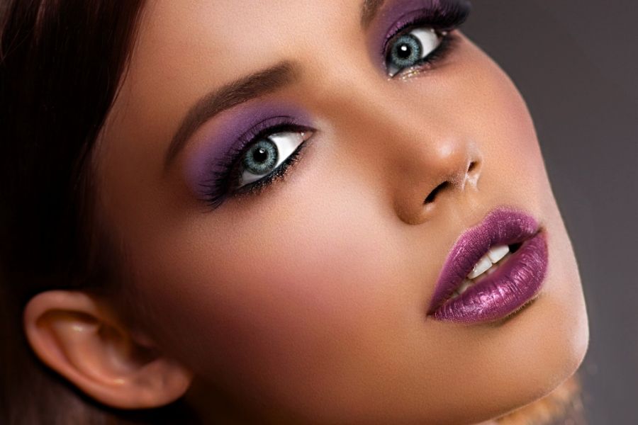 Woman wearing bold Christmas party makeup with purple eyeshadow, winged eyeliner and matching purple lipstick
