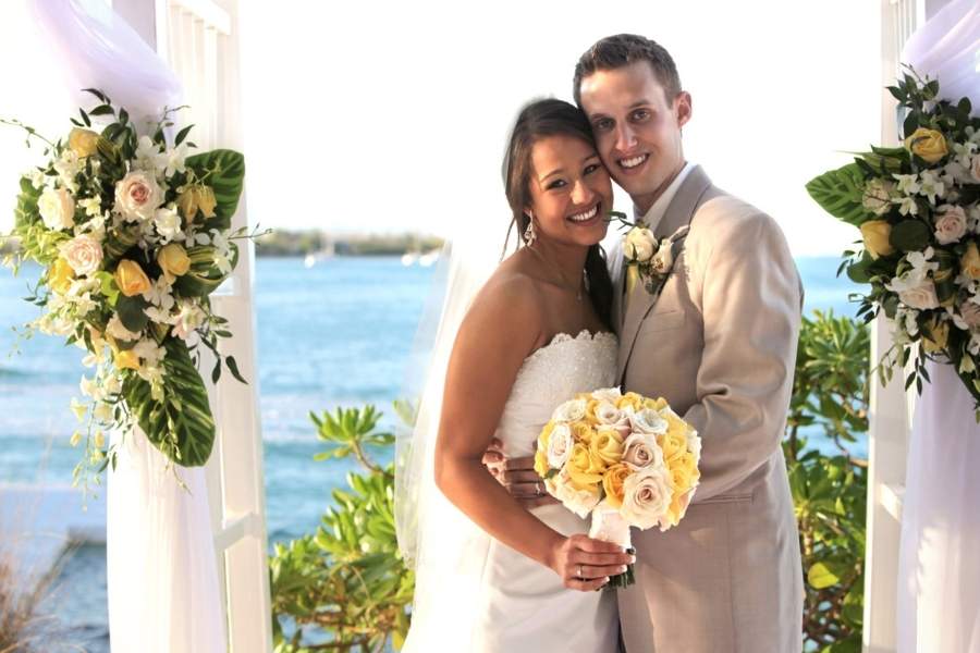 Happy couple at tropical destination wedding ceremony with ocean view and floral arch decorations
