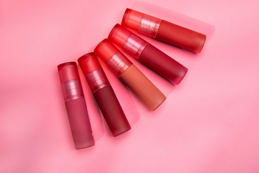 Collection of liquid lipstick tubes in various red shades on pink background
