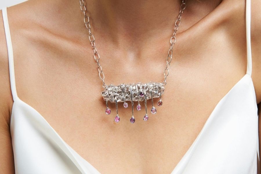 Woman wearing elegant statement earrings with silver chain and pink gemstone dangles against white top