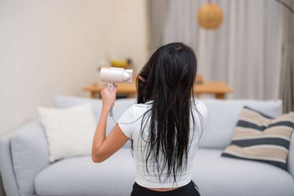 Woman drying her long hair with a hair dryer at home, showing the importance of Hot Tool Safety.