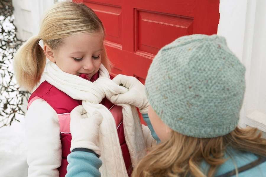 Child learning basic scarf tying methods with help from another person in winter setting