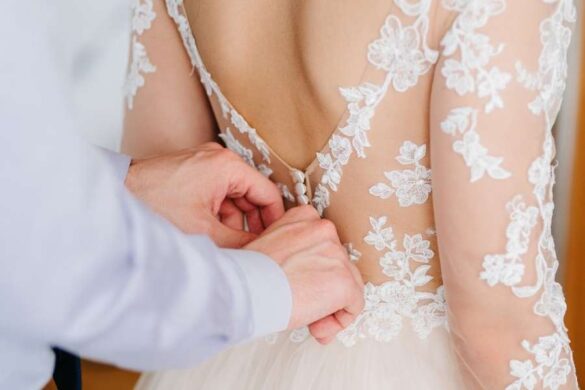 Hands fastening intricate lace wedding dress showcasing wedding day beauty preparation details