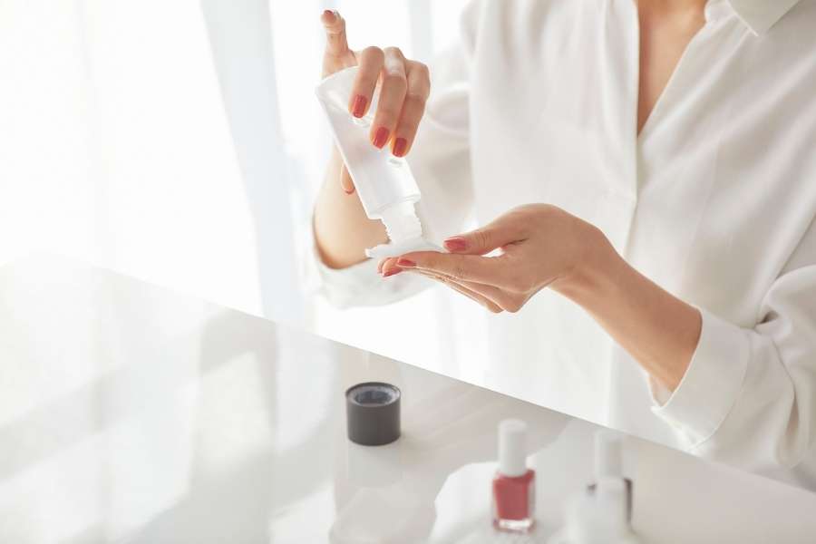 Woman dispensing liquid product onto a cotton pad before cream blush application.