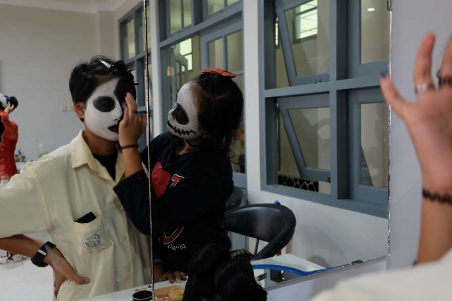 Two people wearing dramatic skull masks demonstrating Halloween special effects makeup techniques in salon mirror