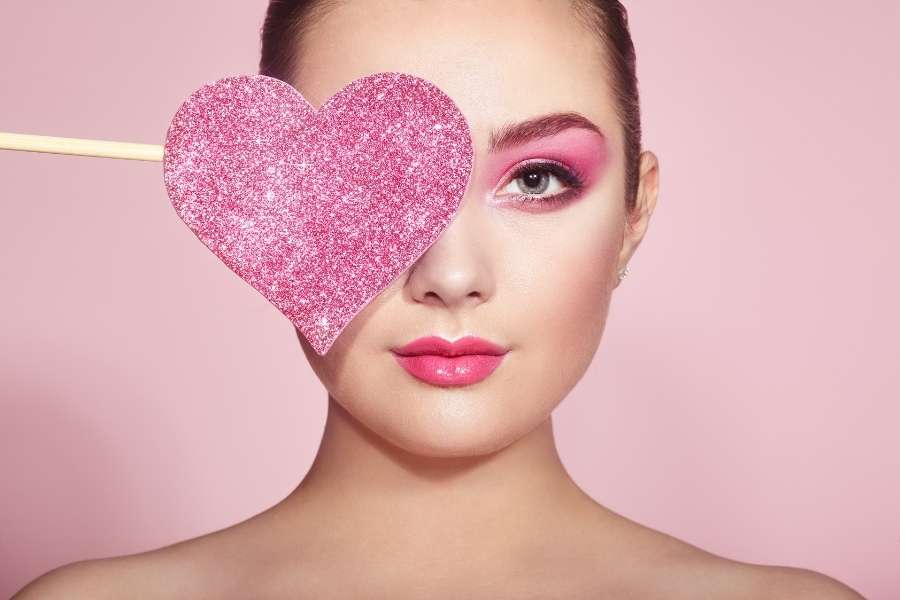Woman with pink eyeshadow and glittery heart prop showcasing romantic Valentine's Day makeup look