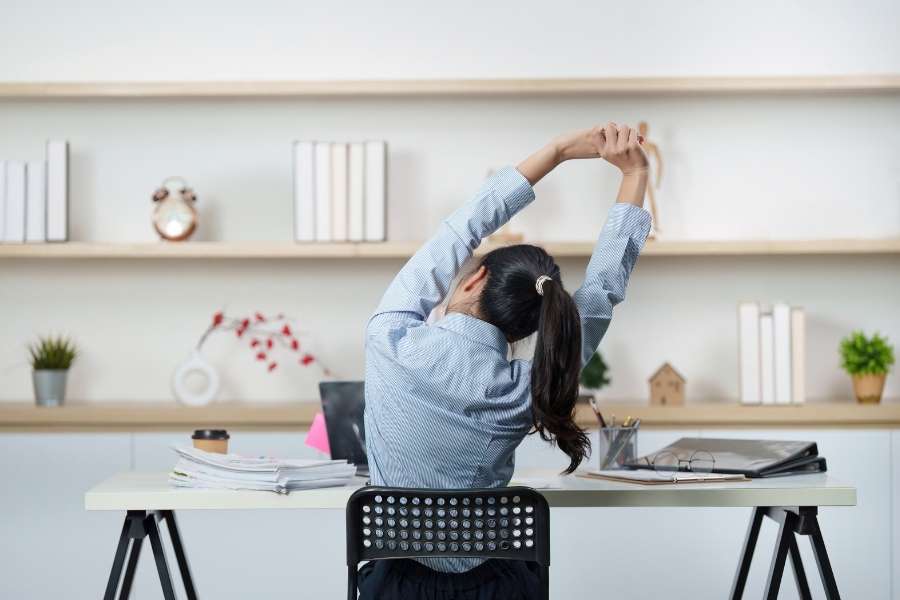An office worker stretching at her desk to help manage daily stress.