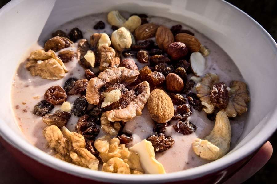 A white bowl filled with creamy yogurt topped with assorted nuts and raisins, featuring healthy snack ideas.